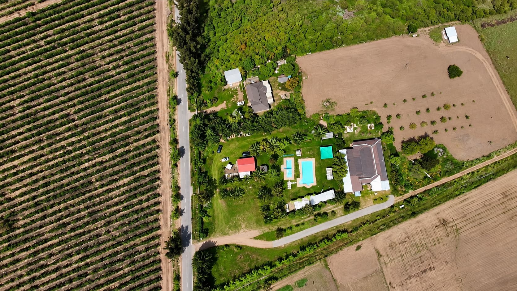 Vista aérea de Pueblo Hundio: las dos piscinas, el salón y los jardines, junto a un camino rural y viñedos