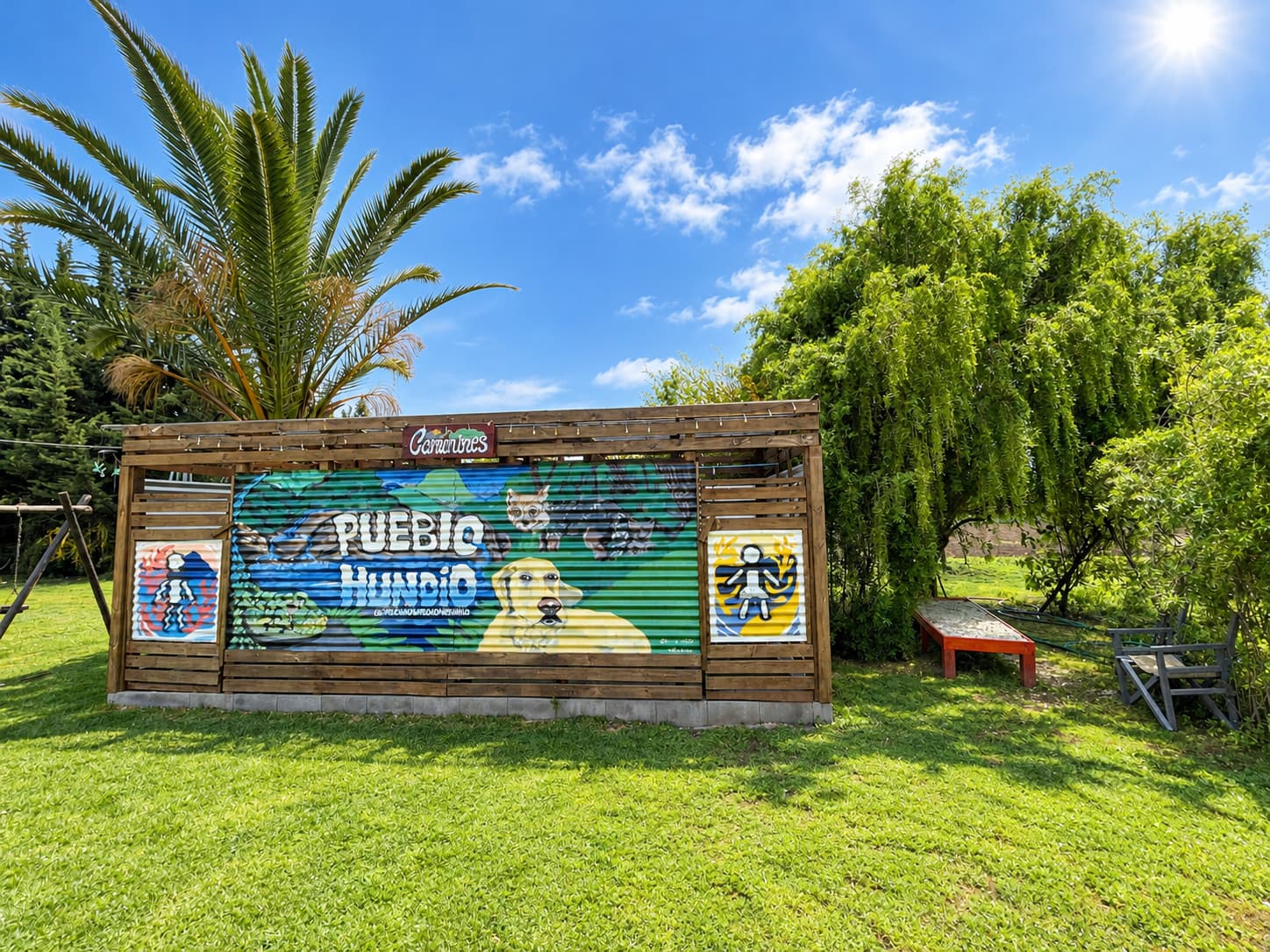 Caseta de madera con un mural colorido de Pueblo Hundio que muestra un perro y un zorro, junto a una palmera