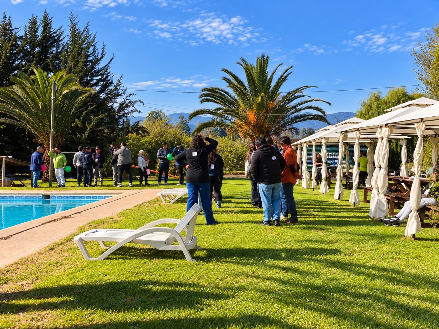 Grupo de personas en una actividad en el pasto junto a la piscina, con palmeras y toldos blancos