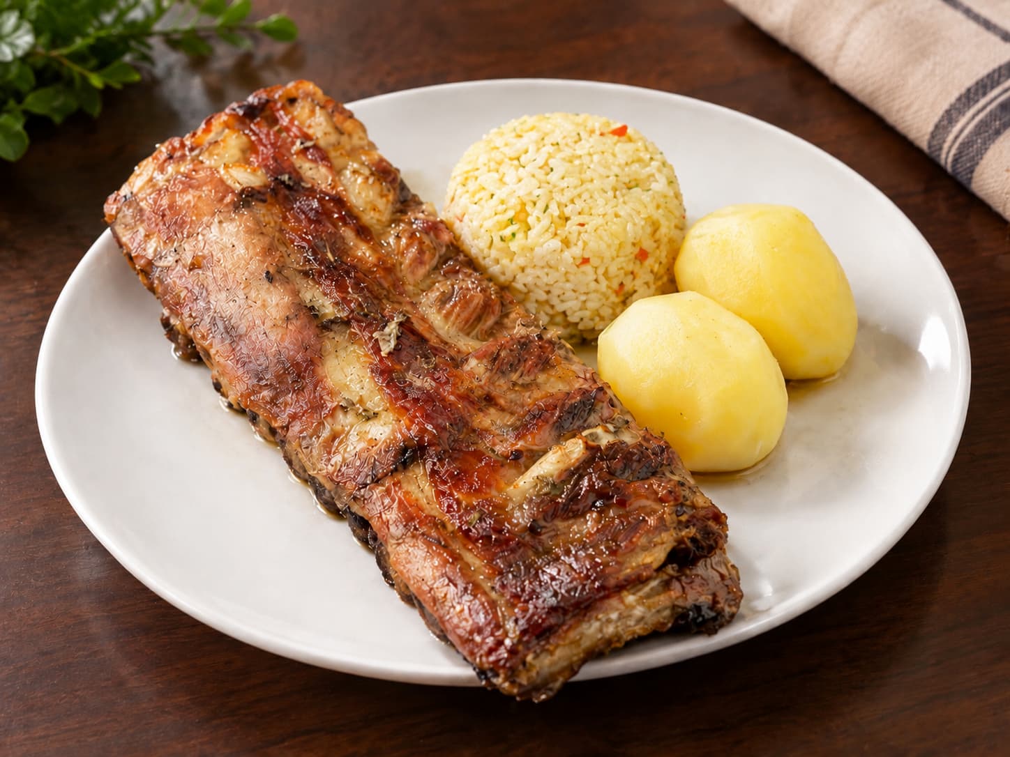 Plato de costillar de cerdo al horno con arroz graneado y dos papas cocidas