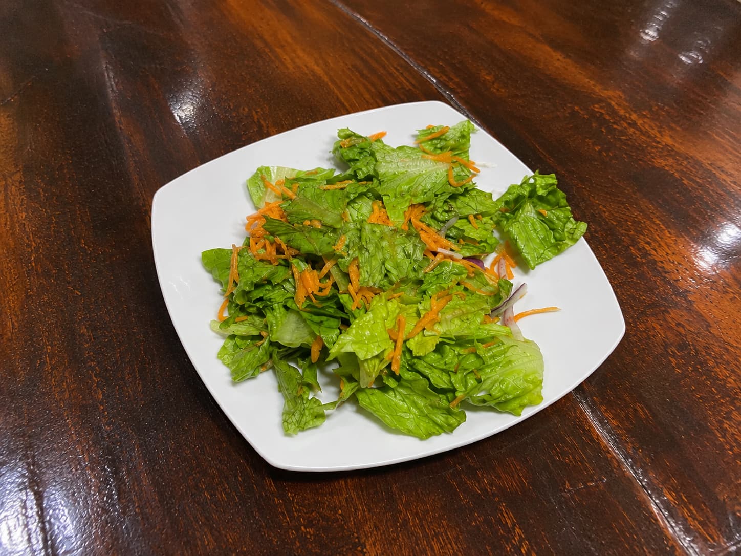 Ensalada fresca de lechuga, zanahoria rallada y cebolla morada en plato blanco cuadrado
