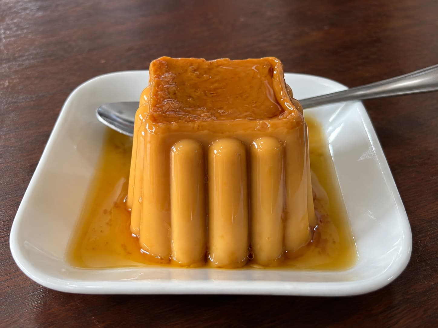 Flan casero con caramelo, en forma de molde acanalado, servido en un plato blanco con cuchara