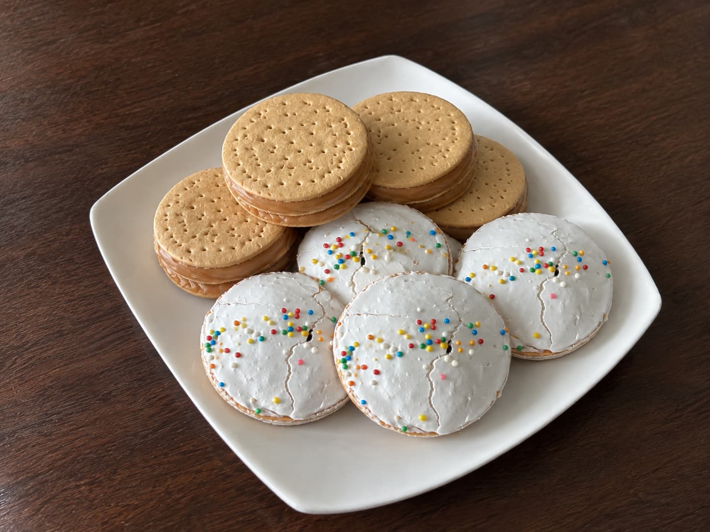 Plato de pastelitos: galletas rellenas de manjar y otras cubiertas de merengue con chispas de colores