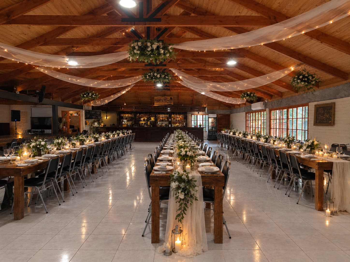 Salón de Pueblo Hundio decorado para un matrimonio, con mesas largas, velas, arreglos de flores blancas y telas con luces en el techo